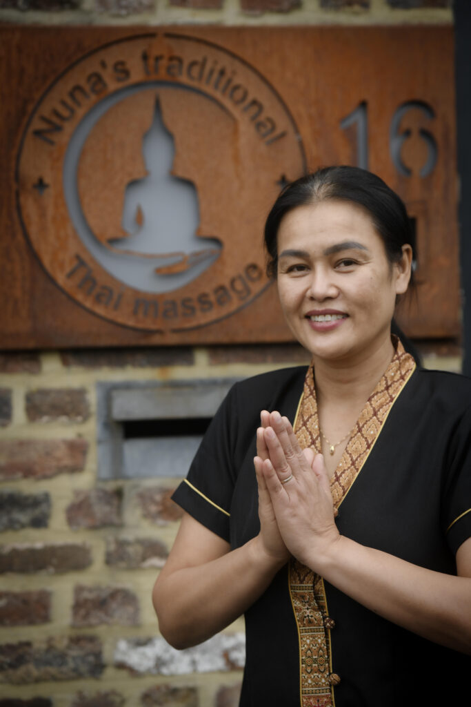 Nuna standing in front of her Nuna's Traditional Thai Massage practice, with the business logo visible.
